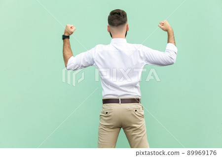Excited businessman celebrates a career achievement. Back view of a young adult businessman, on light green background. Indoor, studio shot 89969176