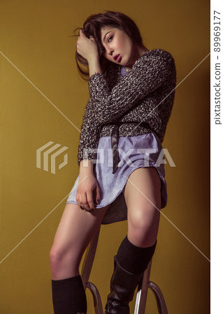 Beautiful young asian model in blue denim skirt and black blouse and fashion makeup posing sitting on stepladder and looking at camera. Studio shot. High-fashion photo. 89969177
