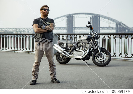 bearded motorcyclist man with his motorbike on summertime posing. bearded motorcyclist man with his motorbike on summertime posing. 89969179