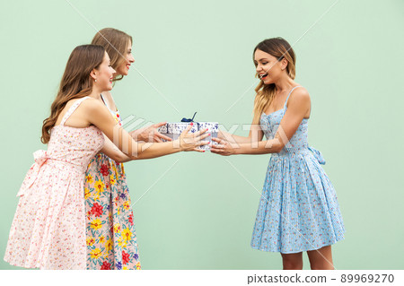 Young adult cute girl giving surprise gift to hes pretty friend. Concept of birthday and party. Isolated on green background Young adult cute girl giving surprise gift to hes pretty friend. Concept of birthday and party. Isolated on green background 89969270