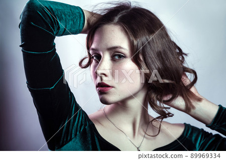 Portrait of beautiful woman with makeup, hairstyle and natural freckles on her face in green dress posing and looking at camera on gray silver background. 89969334
