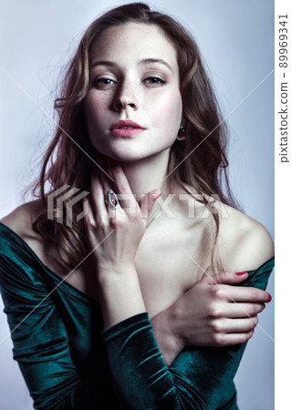 Portrait of beautiful woman with makeup, hairstyle and natural freckles on her face in green dress posing and looking at camera on gray silver background. Portrait of beautiful woman with makeup, hairstyle and natural freckles on her face in green dress posing and looking at camera on gray silver background. 89969341