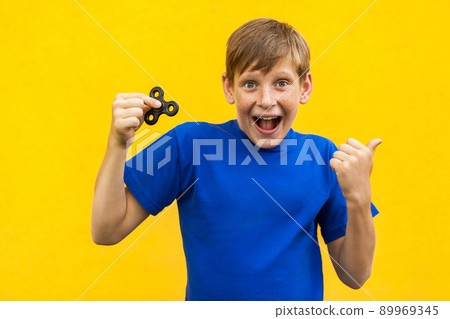 Young beautiful happy boy with freckles blue t-shirt holding fidget spinner on yellow background with amazed face.. 89969345