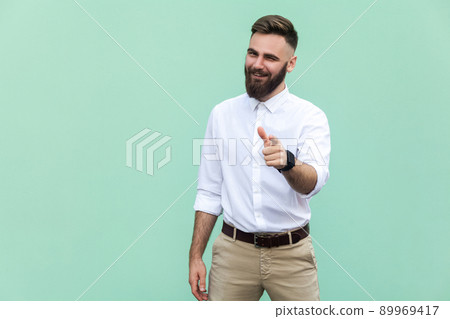 Hey you! Young adult bearded man, pointing finger and looking at camera. On light green background. Indoor, studio shot 89969417