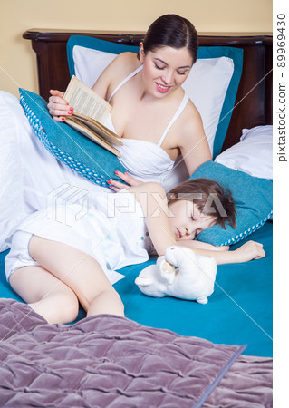 Daughter sleeping, mom read book and looking for child. Studio shot 89969430