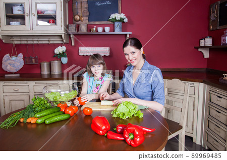 Happy mother and daughter enjoy making and having healthy meal together at their kitchen. they are making vegetable salad and having fun together. mom take care of her daughter and tech how to cook. Happy mother and daughter enjoy making and having healthy meal together at their kitchen. they are making vegetable salad and having fun together. mom take care of her daughter and tech how to cook. 89969485