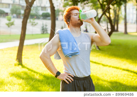 Young adult redhead and freckles man, drink water after cross and closed eyes. Outdoor Young adult redhead and freckles man, drink water after cross and closed eyes. Outdoor 89969486