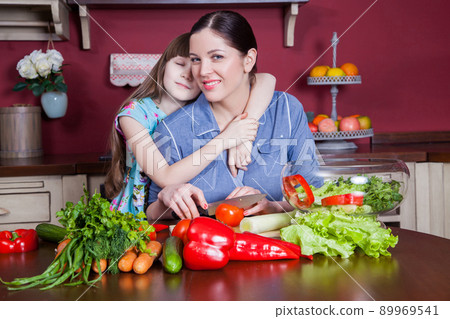 Happy mother and daughter enjoy making and having healthy meal together at their kitchen. they are making vegetable salad and having fun together. mom take care of her daughter and tech how to cook. Happy mother and daughter enjoy making and having healthy meal together at their kitchen. they are making vegetable salad and having fun together. mom take care of her daughter and tech how to cook. 89969541