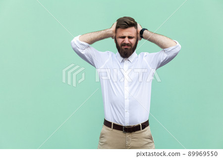 Pain in head. Pained businessman, has a headache, isolated on light green background. Indoor, studio shot Pain in head. Pained businessman, has a headache, isolated on light green background. Indoor, studio shot 89969550