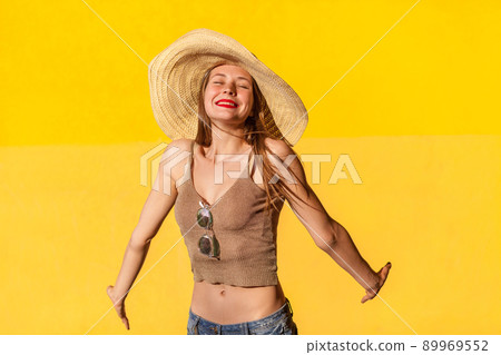 Portrait of cute young adult model in straw hat. Closed eyes and toothy smile. Isolated on yellow background Portrait of cute young adult model in straw hat. Closed eyes and toothy smile. Isolated on yellow background 89969552
