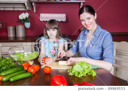 Happy mother and daughter enjoy making and having healthy meal together at their kitchen. they are making vegetable salad and having fun together. mom take care of her daughter and tech how to cook. Happy mother and daughter enjoy making and having healthy meal together at their kitchen. they are making vegetable salad and having fun together. mom take care of her daughter and tech how to cook. 89969553