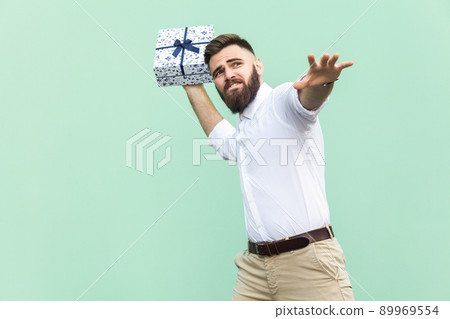 Catch your gift! Young adult man swung and wants to throw off your gift box, isolated on light green background. Studio shot Catch your gift! Young adult man swung and wants to throw off your gift box, isolated on light green background. Studio shot 89969554