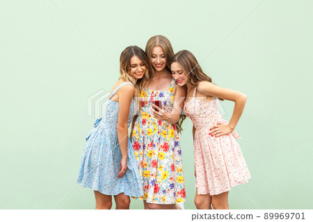 Meeting three best friends. One girl shows image or video on screen of smart phone. Others girls looking on screen phone and smiling. Isolated on green background, studio shot Meeting three best friends. One girl shows image or video on screen of smart phone. Others girls looking on screen phone and smiling. Isolated on green background, studio shot 89969701