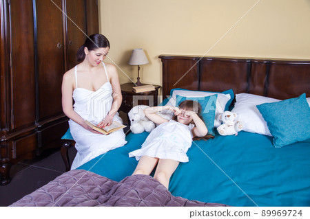 Beautiful little girl rub eyes and going to sleep. Mom looking for daughter and toothy smile. Studio shot 89969724