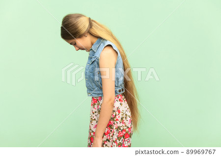 Side view of sad teenager girl, punished alone at green wall. Indoor studio shoot Side view of sad teenager girl, punished alone at green wall. Indoor studio shoot 89969767