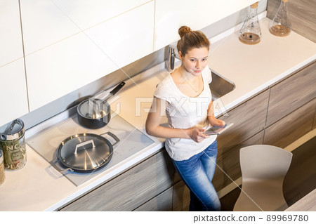 Beautiful young woman using a digital tablet in the kitchen. 89969780