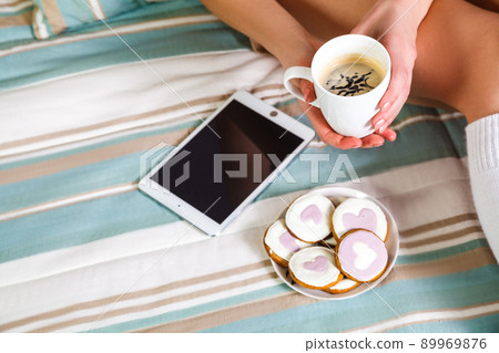 Woman using tablet at cozy home atmosphere on the bed. Young woman with cup of cocoa or coffee in hands enjoying free time with comfort. Soft light and comfy lifestyle concept. top view point.. Woman using tablet at cozy home atmosphere on the bed. Young woman with cup of cocoa or coffee in hands enjoying free time with comfort. Soft light and comfy lifestyle concept. top view point.. 89969876