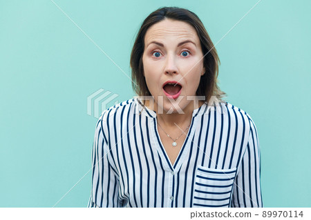 Wow! Amazed and shocked beautiful adult lady looking at camera with shocked face. Isolated on light blue background. Wow! Amazed and shocked beautiful adult lady looking at camera with shocked face. Isolated on light blue background. 89970114