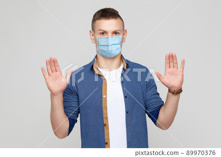 Stop. Portrait of serious young man in casual style with medical mask standing with stop sign and looking at camera. medical and health care concept. indoor studio shot, isolated on gray background. 89970376