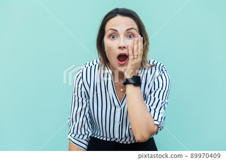 No way! Surprised business woman lady with opened mouth and big eyes. Looking at camera and touching her face. Isolated on blue background, studio shot No way! Surprised business woman lady with opened mouth and big eyes. Looking at camera and touching her face. Isolated on blue background, studio shot 89970409
