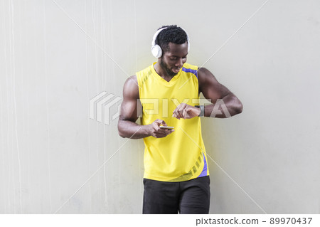 dark skinned sporty man holding smart phone and looking at smart watch. Outdoor shot, morning. Spring or summer dark skinned sporty man holding smart phone and looking at smart watch. Outdoor shot, morning. Spring or summer 89970437