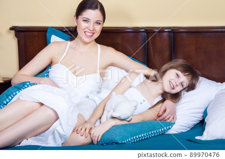 Happiness mom and her beautiful girl lie in bed in the morning, hugging , toothy smiling an looking at camera. Studio shot Happiness mom and her beautiful girl lie in bed in the morning, hugging , toothy smiling an looking at camera. Studio shot 89970476
