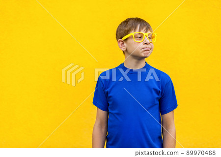 Dissatisfied and unhappy boy in yellow glasses, loking away. Isolated on yellow wall, studio shot Dissatisfied and unhappy boy in yellow glasses, loking away. Isolated on yellow wall, studio shot 89970488
