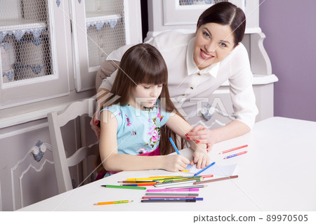 Happy beautiful mother teach her daughter to paint, painting and smiling and looking at camera. Studio shot. Happy beautiful mother teach her daughter to paint, painting and smiling and looking at camera. Studio shot. 89970505