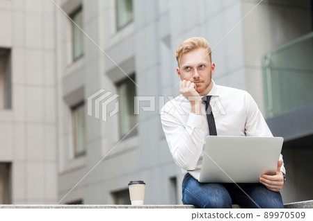 Working in outdoor, sits on the ground. Young adult ginger bearded businessman , work in computer and dreaming. Outdoor shot Working in outdoor, sits on the ground. Young adult ginger bearded businessman , work in computer and dreaming. Outdoor shot 89970509
