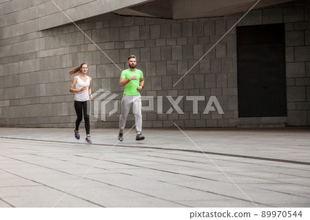 Active happy young couple jogging side by side in an urban street during their daily workout in a health and fitness concept. using sport watch. 89970544
