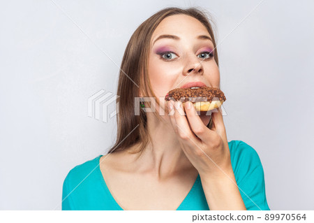 Portrait of beautiful girl with chocolate donuts. eating and looking at camera. studio shot on light gray background. 89970564