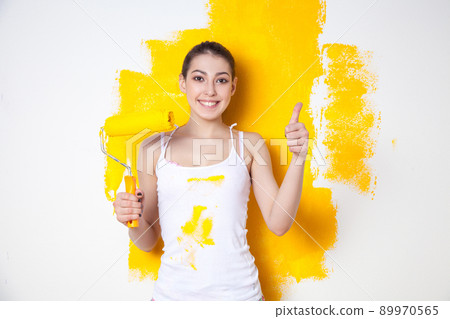 Beautiful young caucasian model in coloured shorts and white shirt and posing holding outrigger in her hands, painting the wall and looking at camera. Studio shot. 89970565