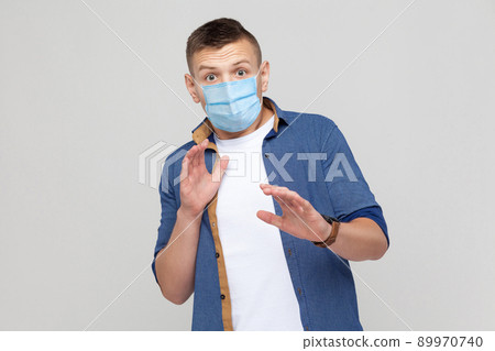 No, wait. Portrait of scared young man in casual style with surgical medical mask standing and looking at camera, afraid and panic. indoor studio shot, isolated on gray background. 89970740