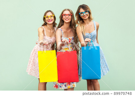 Portrait of three pretty happy girls with packages with new clothes. Showing packets and looking with toothy smile at camera. Studio shot. Green background Portrait of three pretty happy girls with packages with new clothes. Showing packets and looking with toothy smile at camera. Studio shot. Green background 89970748