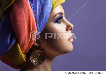 Beautiful woman with colored headwear and blue makeup, studio shot on purple background Beautiful woman with colored headwear and blue makeup, studio shot on purple background 89970828