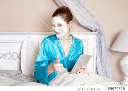 Beautiful woman with green nightie and white facial mask resting on bed and holding tablet before sleeping. healthcare and beauty treatment and technology concept. studio shot. . 89970829