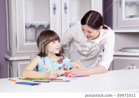 Happy beautiful mother teach her daughter to paint, painting and smiling and looking at camera. Studio shot. Happy beautiful mother teach her daughter to paint, painting and smiling and looking at camera. Studio shot. 89971011