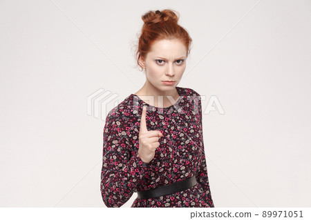 Warning sign. Ginger woman looking at camera with serious face and finger warning. Studio shot, on gray background. 89971051