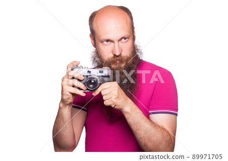 The portrait of bald bearded man photographer with pink t shirt holding classic camera. isolated on white background. studio shot. The portrait of bald bearded man photographer with pink t shirt holding classic camera. isolated on white background. studio shot. 89971705