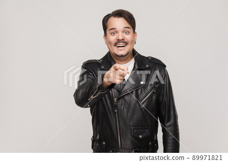 The happiness man, wearing black jacket, having happiness looks, pointing finger at camera and toothy smiling. Isolated studio shot on gray background The happiness man, wearing black jacket, having happiness looks, pointing finger at camera and toothy smiling. Isolated studio shot on gray background 89971821