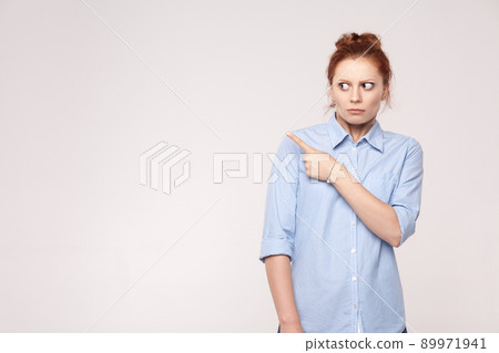 Scared redhead woman pointing away while standing isolated on gray background. Studio shot Scared redhead woman pointing away while standing isolated on gray background. Studio shot 89971941