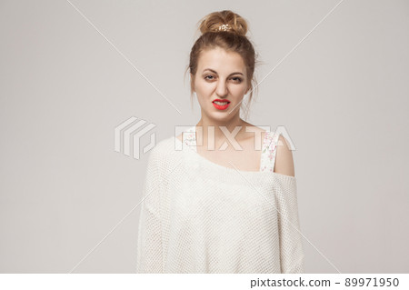 Blonde woman looking at camera with disgust. Studio shot, gray wall 89971950