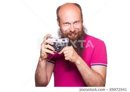 The portrait of bald bearded man photographer with pink t shirt holding classic camera. isolated on white background. studio shot. The portrait of bald bearded man photographer with pink t shirt holding classic camera. isolated on white background. studio shot. 89972041