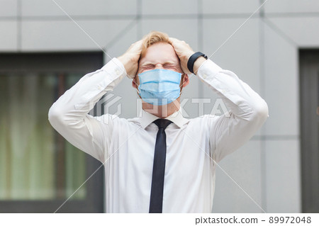 Bad emotions and feelings concept. Headache. Businessman with surgical medical mask touching head and have a migraine or problem with work. Outdoor shot. business, working and health care concept. Bad emotions and feelings concept. Headache. Businessman with surgical medical mask touching head and have a migraine or problem with work. Outdoor shot. business, working and health care concept. 89972048