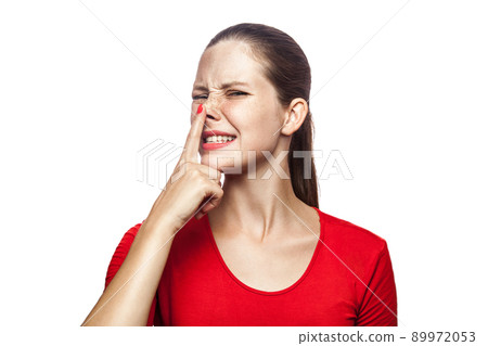 Portrait of liar woman in red t-shirt with freckles. looking up and touch her nose, studio shot. isolated on white background. 89972053