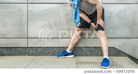 Knee ache and sport injury. Young man holding his painful knee and feeling bad. sport and healthcare lifestyle concept. cropped and standing on gray wall. outdoor shot, closeup. Knee ache and sport injury. Young man holding his painful knee and feeling bad. sport and healthcare lifestyle concept. cropped and standing on gray wall. outdoor shot, closeup. 89972056