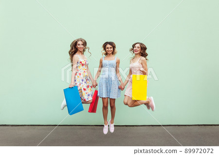 Happiness beautiful three friends jumping from happy with colorful packets after shopping. Outdoor. Green wall 89972072