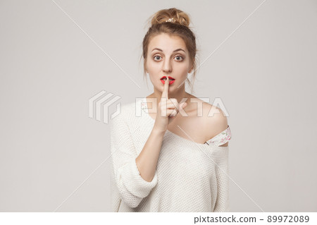 Secrecy sign. Blone woman with big eyes, showing secret shh sign. Studio shot, isolated on gray background Secrecy sign. Blone woman with big eyes, showing secret shh sign. Studio shot, isolated on gray background 89972089