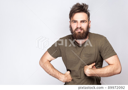 Portrait of funny crazy bearded man with dark green t shirt against light gray background. studio shot. . Portrait of funny crazy bearded man with dark green t shirt against light gray background. studio shot. . 89972092