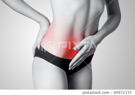 Closeup view of a young woman with stomach pain or digestion or period cycle on gray background. Black and white photo with red dot. 89972155